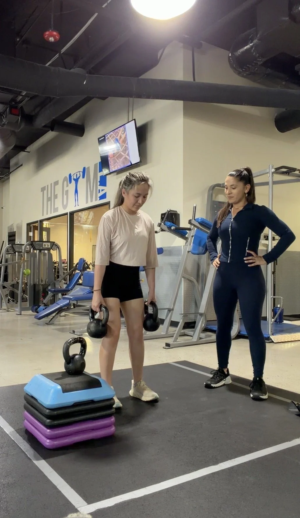 Shira coaching a client through a strength exercise in the gym