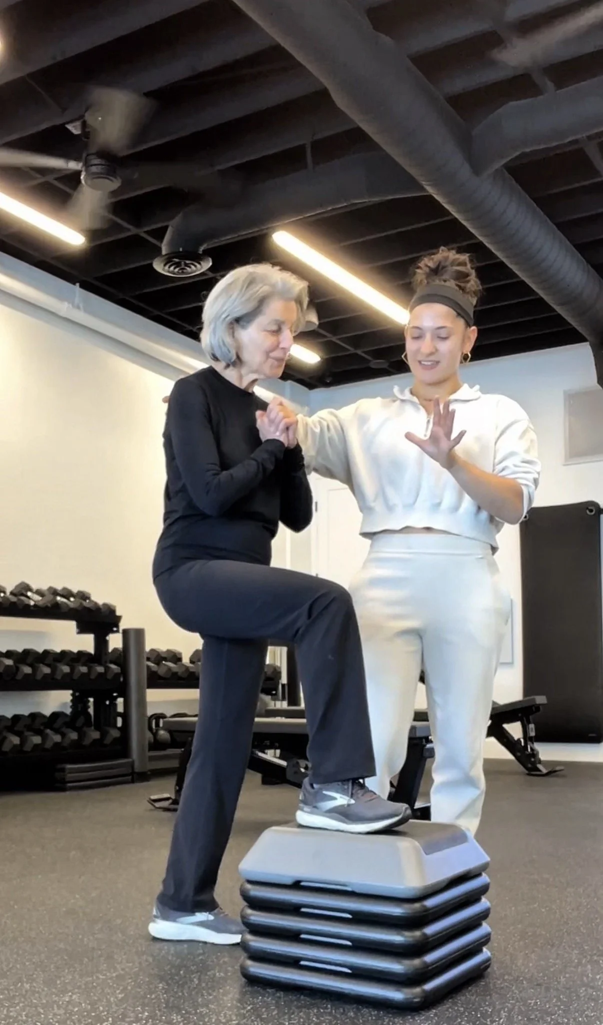 Trainer steadying an older client through a step-up in the gym